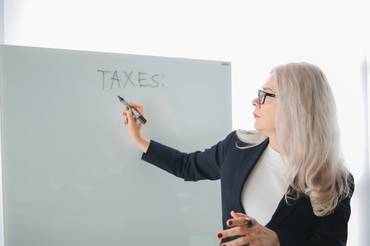 Senior woman writing on whiteboard during a tax discussion in office setting.